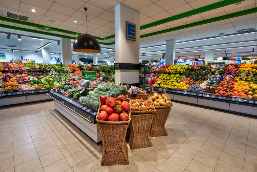 Weitwinkelaufnahme der Obst- und Gemüseabteilung eines EDEKA-Markts mit großen Auslagen und Körben im Vordergrund.