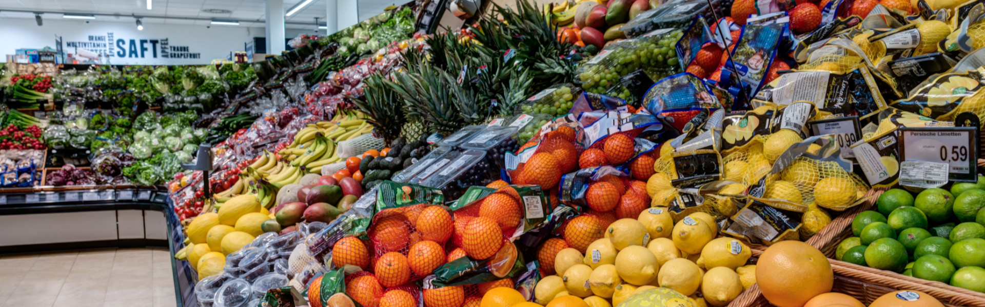 Große Obst- und Gemüseauslage im Supermarkt mit Zitrusfrüchten, Melonen, Ananas, Bananen und Trauben.